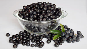Aronia berries in a glass bowl and scattered on table
