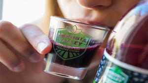 woman drinking aronia berry juice out of an Akronia Valley logo shot glass, the shield for healthy living